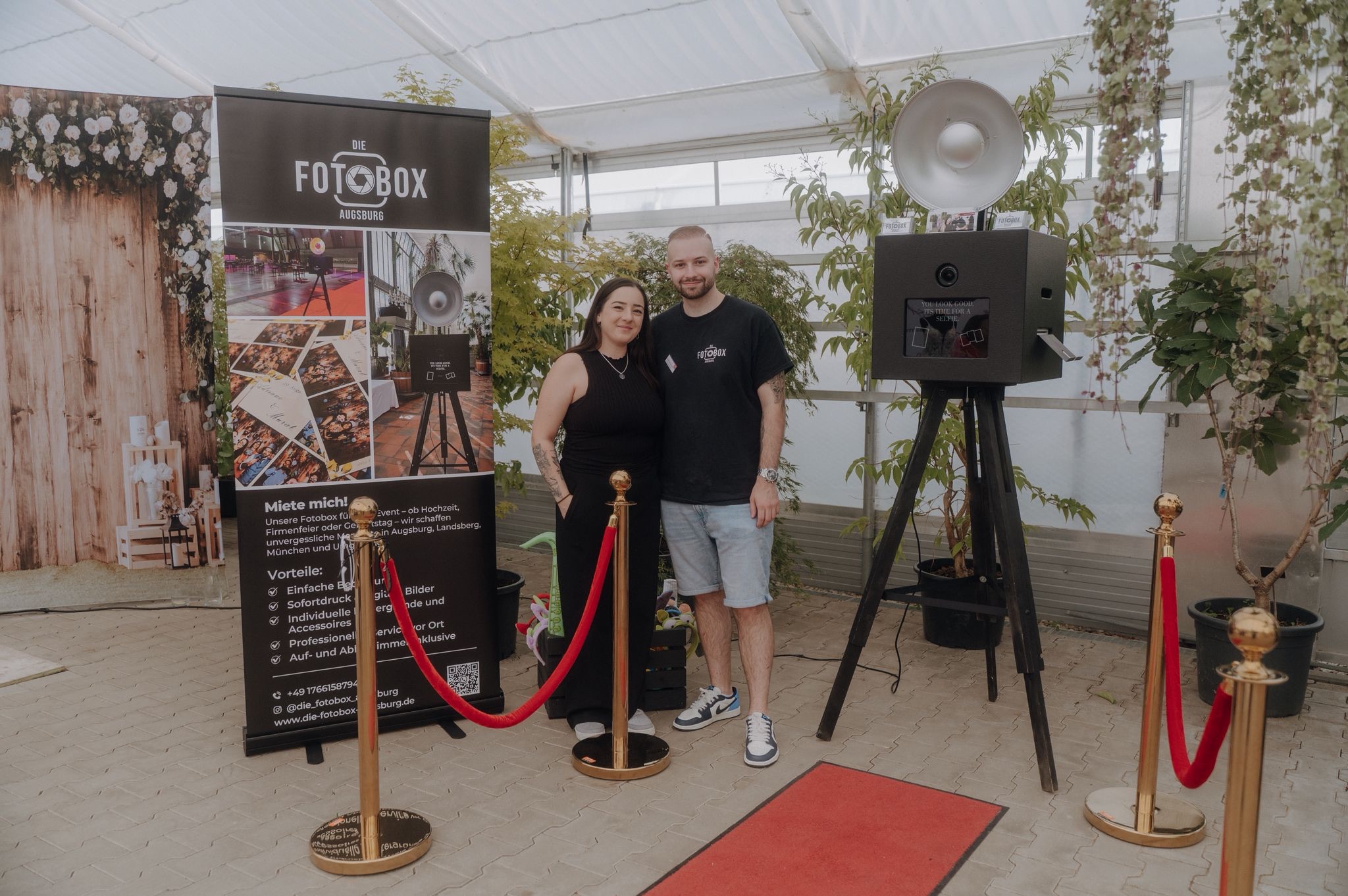 Chris und Alessandra, Gründer und Inhaber von Die Fotobox Bayern, neben einer professionellen Fotobox auf einem Event.